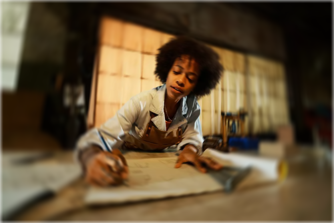 A young maker focused at her workbench, sketching plans by lamplight
